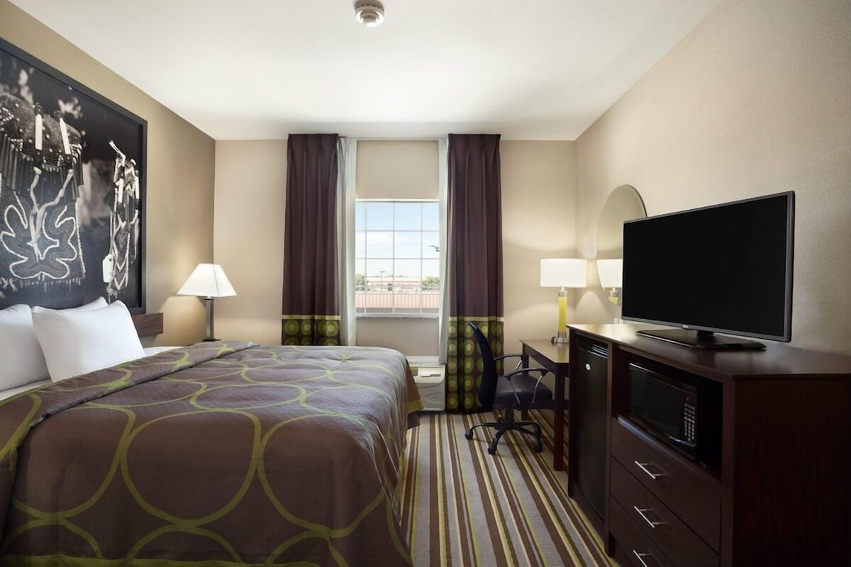 A hotel room with a bed, a desk, a television, a microwave, and a window with curtains.