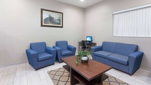 A living room with two blue sofas, a coffee table, a framed picture on the wall, and a window with blinds. - Super 8 by Wyndham Bakersfield South CA (Bakersfield)