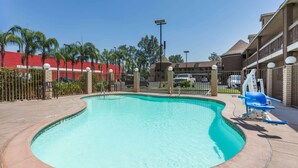 A swimming pool with a curved edge, surrounded by a fence, and adjacent to a building with a red exterior and balconies. - Super 8 by Wyndham Bakersfield South CA (Bakersfield)