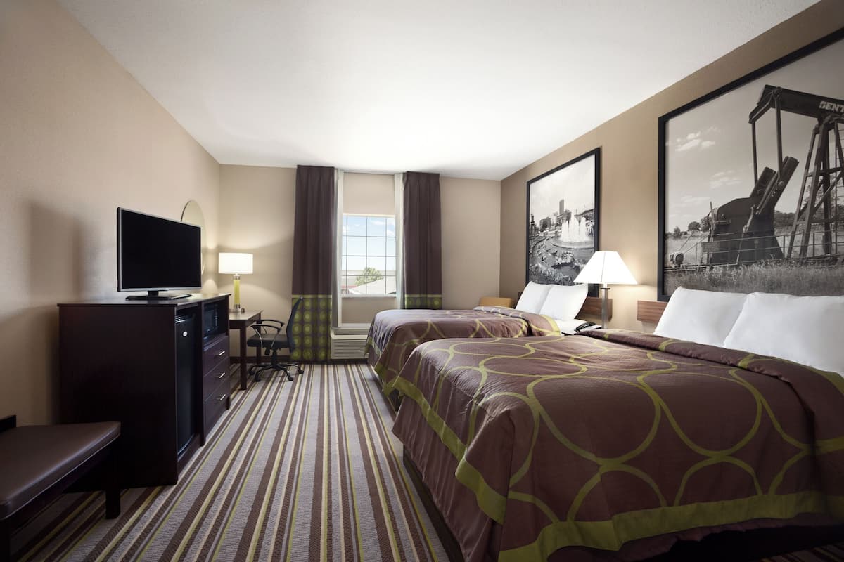 Ein Hotelzimmer mit zwei Betten, einem Schreibtisch mit Fernseher, einem Sessel, einer Lampe und einem großen Fenster.
