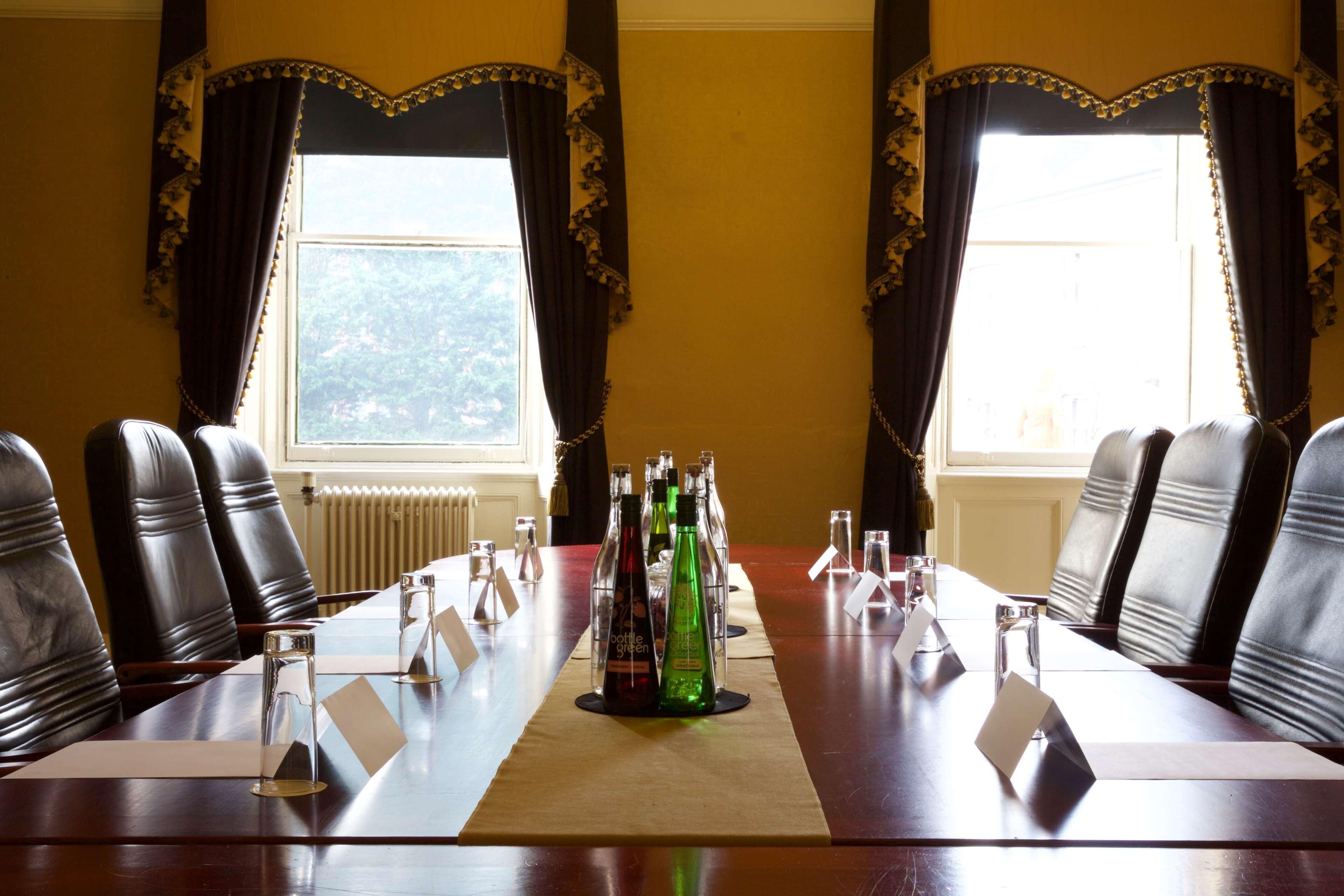 Un salón de conferencias con una mesa larga, sillas y un ventanal con cortinas.