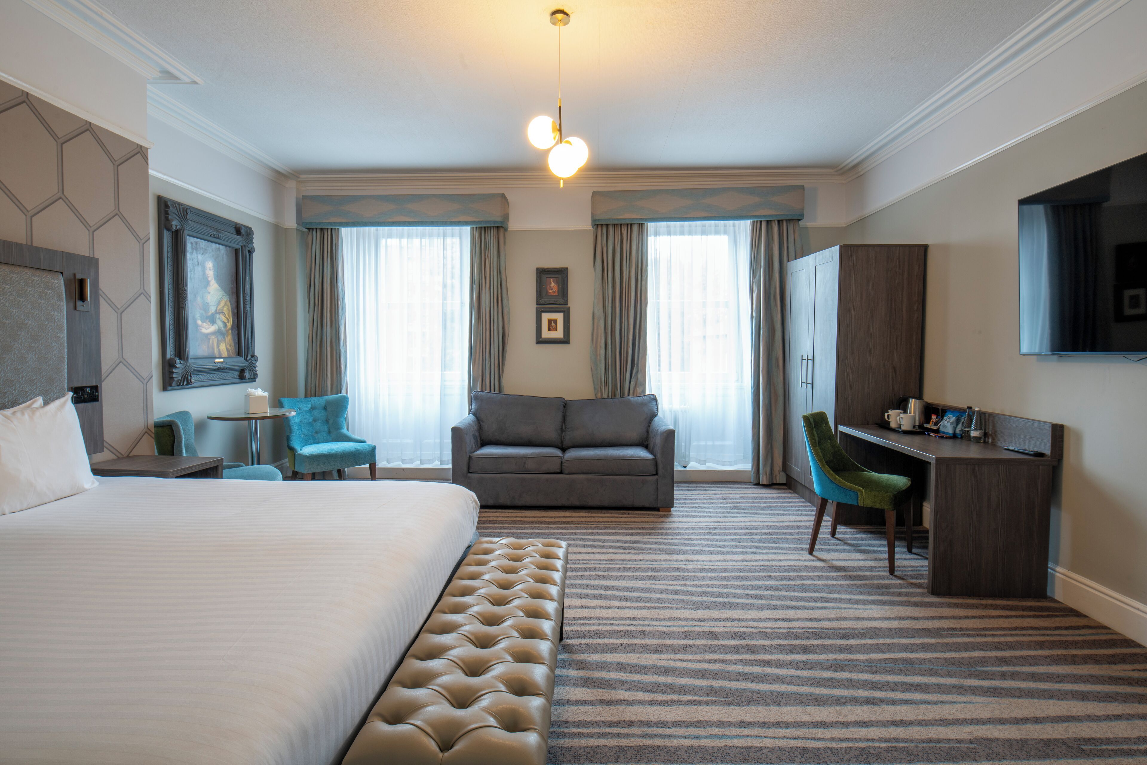 A hotel room with a large bed, a sofa, a desk, and a television.