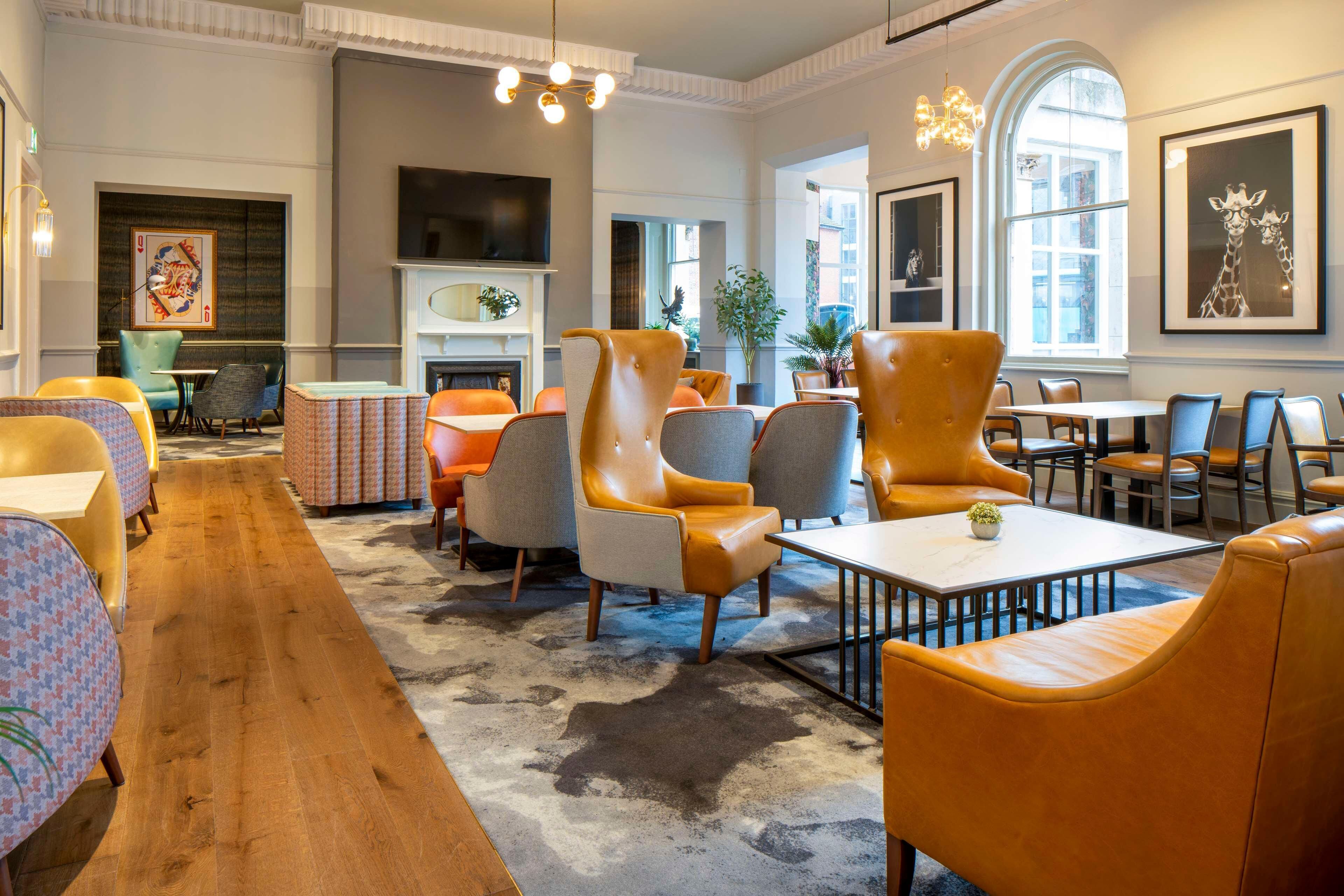 A hotel lobby with leather armchairs, a fireplace, a television, and a large window.