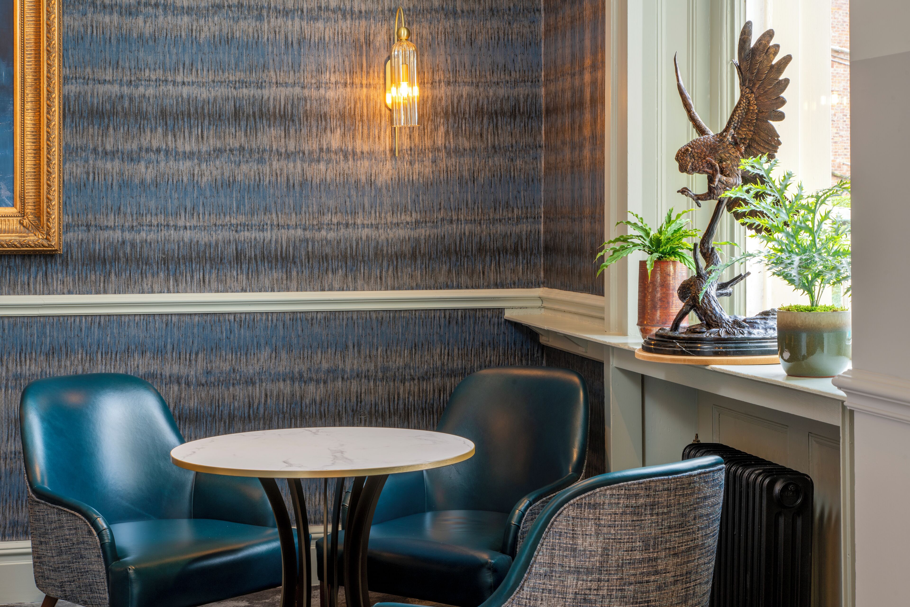 A room with a round table, two blue chairs, a decorative wall, a hanging light fixture, and a statue.