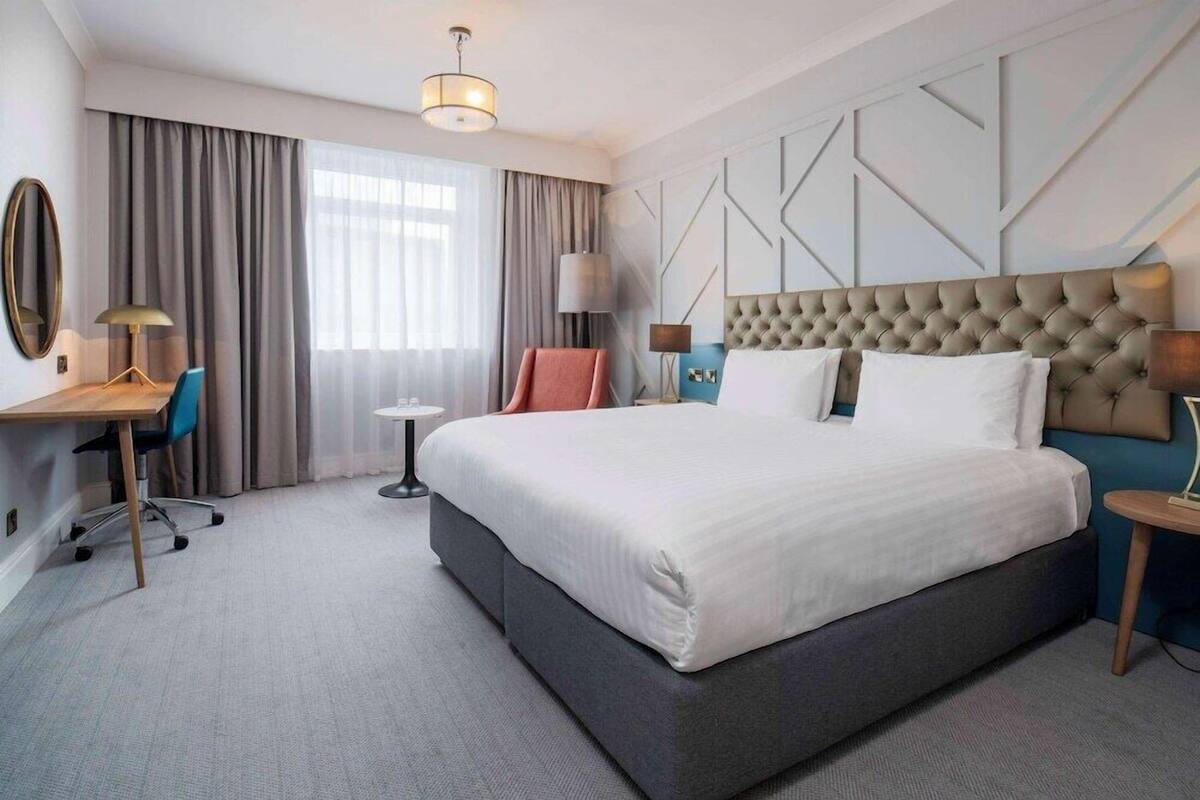 Una habitación de hotel con una cama grande, un escritorio, una silla y una mesita.