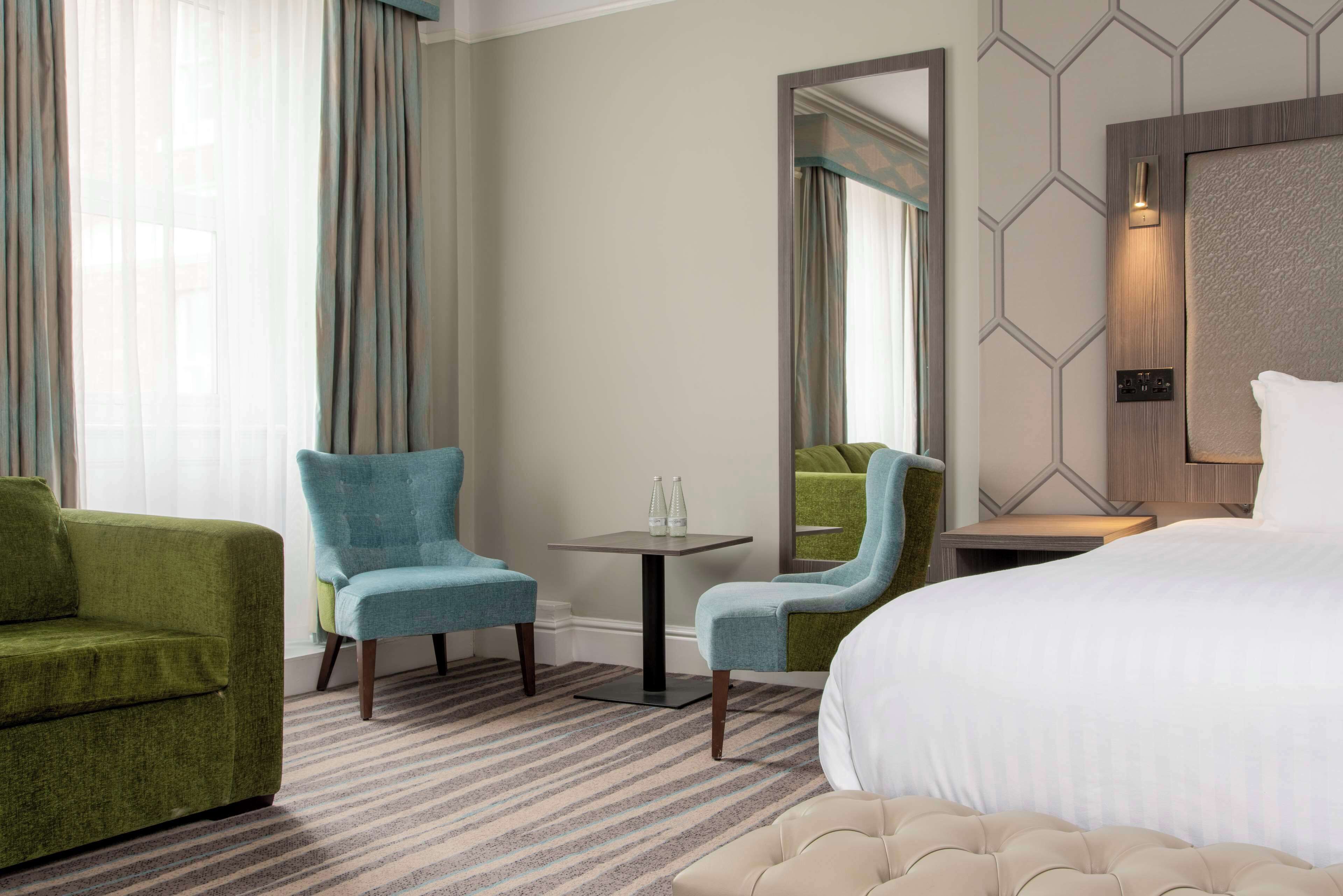 A hotel room with a bed, two armchairs, a small table, and a mirror.