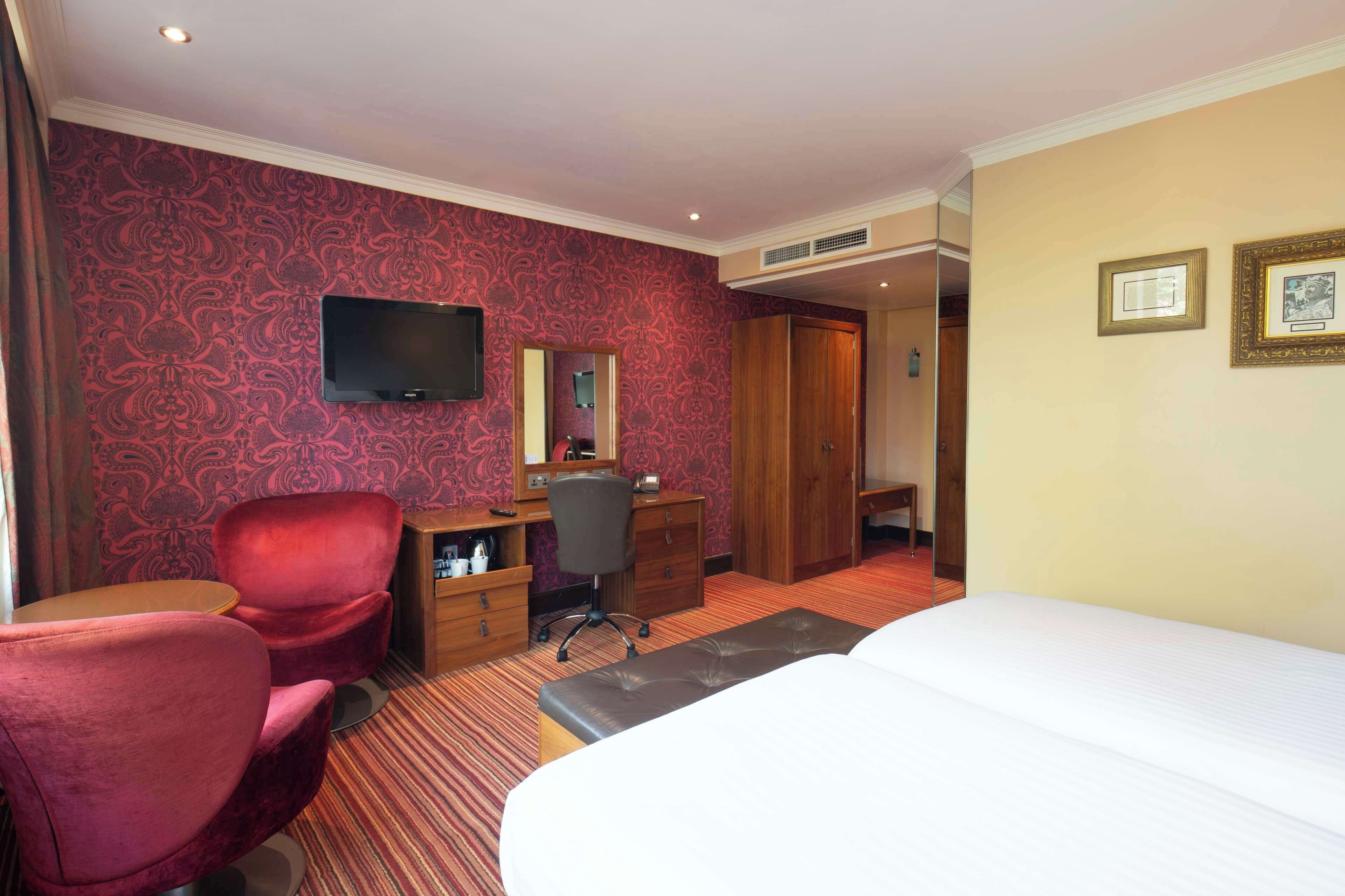 A hotel room with a bed, a desk with a chair, a TV, and a mirror.