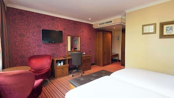 A hotel room with a bed, a desk with a chair, a TV, and a mirror.