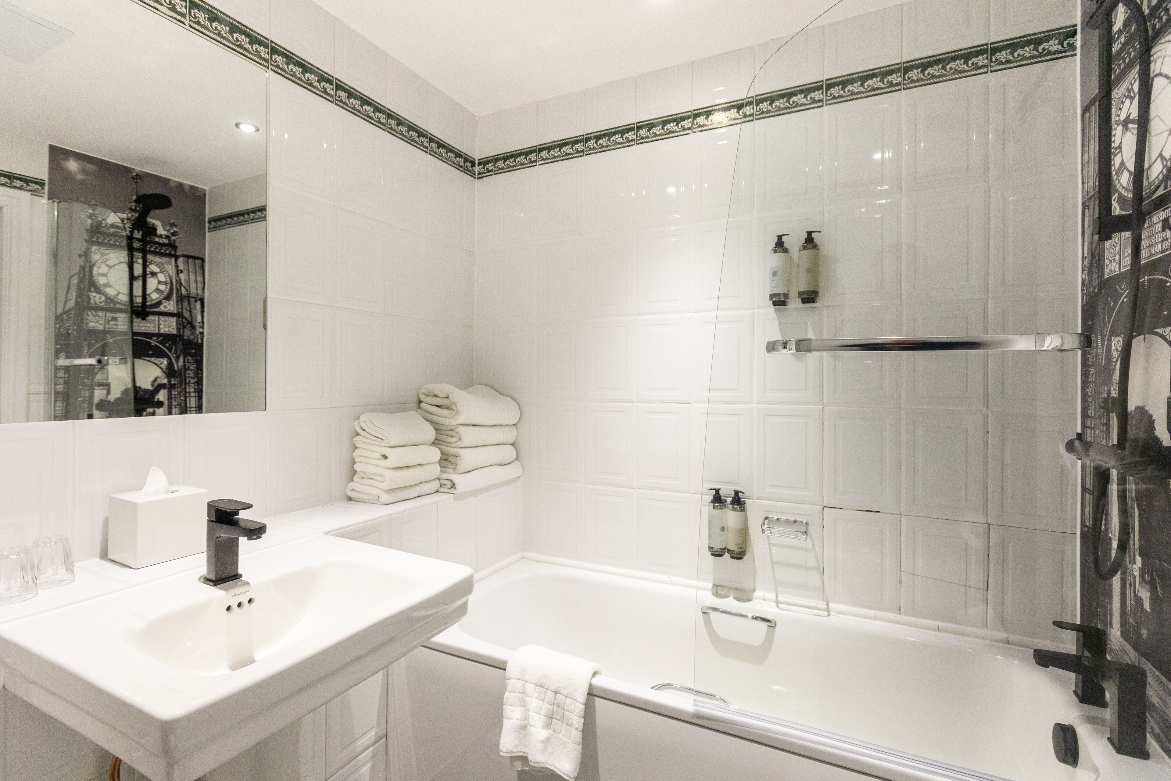 A bathroom with a white sink, a mirror, a bathtub, and a stack of white towels.