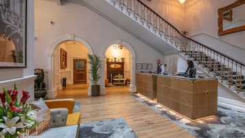 Un'ampia hall con un'imponente scalinata, una reception e un'area salotto con un tavolino.