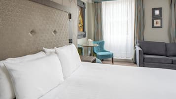 Une chambre d’hôtel avec un grand lit, une petite table ronde, un fauteuil bleu, un canapé gris et un tableau au mur.