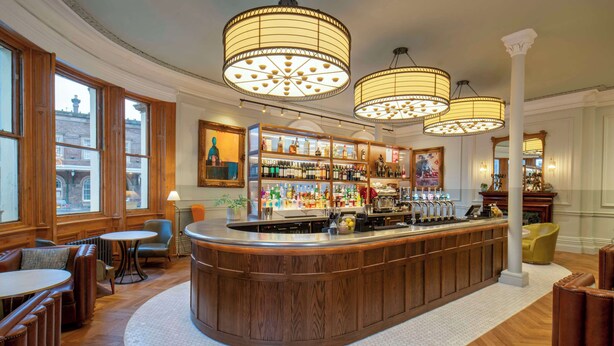 A bar area with wooden furniture, a round bar counter, and hanging lamps. - The Queen at Chester Hotel - Handwritten Collection (Chester)