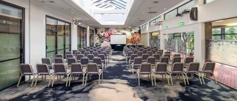 Un salón de conferencias con filas de sillas, una pizarra y un ventanal grande.