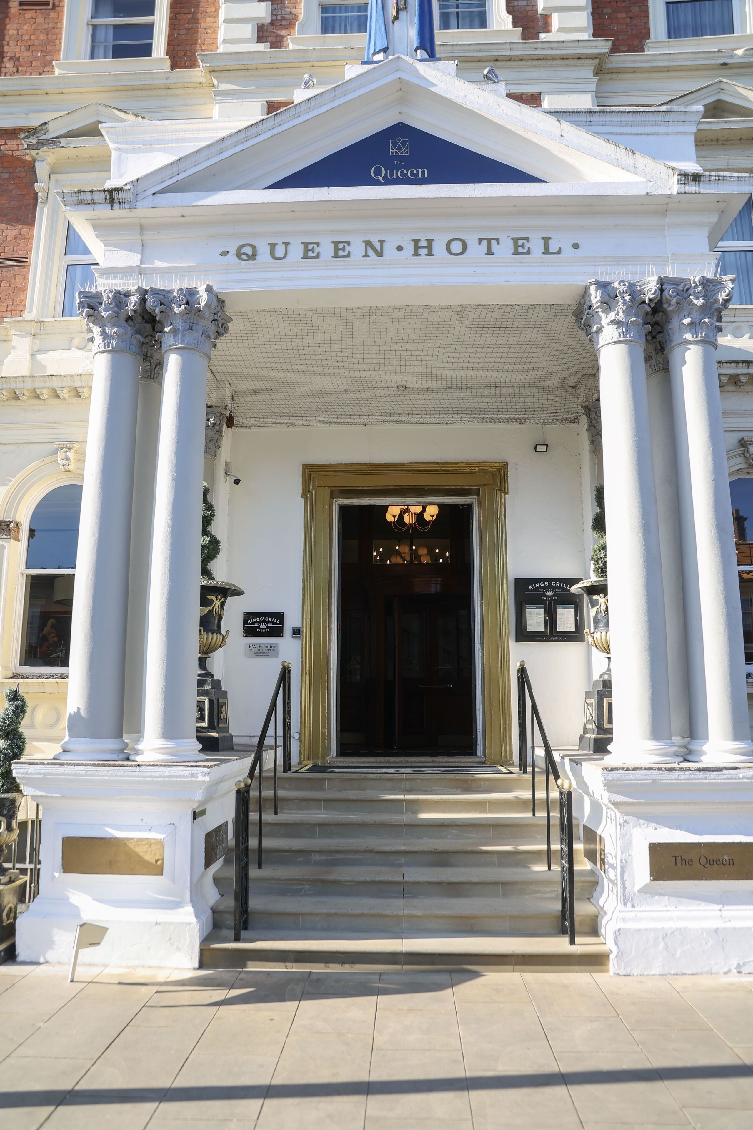 The entrance to the Queen Hotel with a classic facade, a grand staircase, and a sign for Kings' Grill.