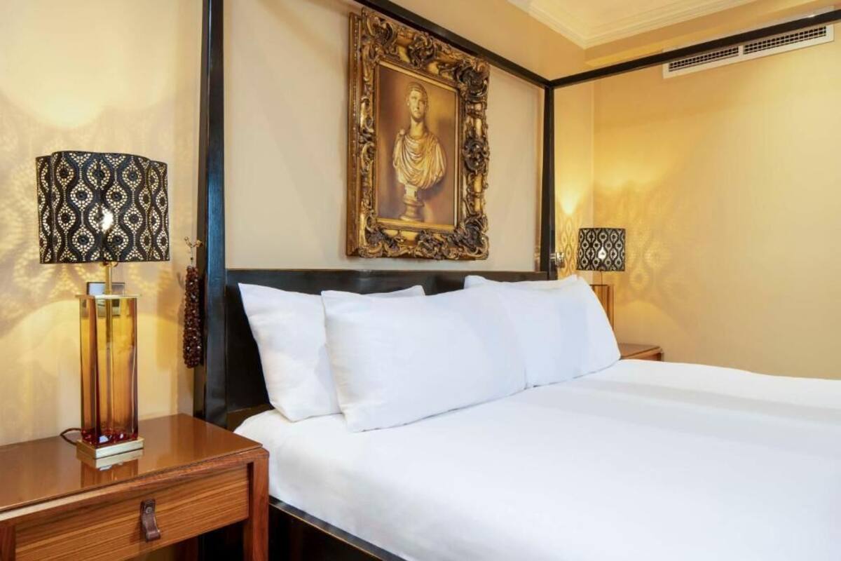 A hotel room with a large bed, two bedside tables, a framed artwork on the wall, and two lamps.