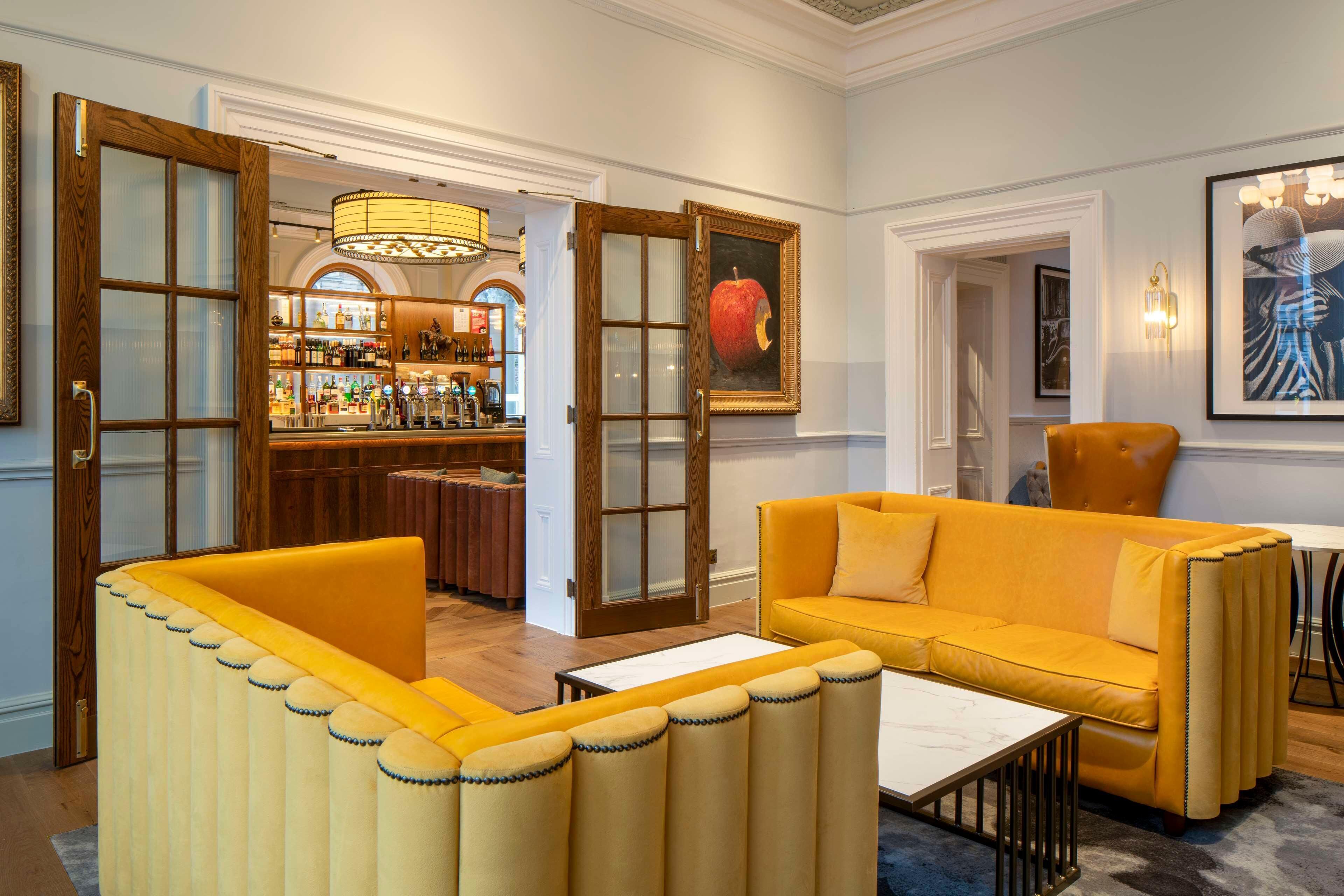 A room with a yellow sofa, a coffee table, and a bar area with shelves of bottles.