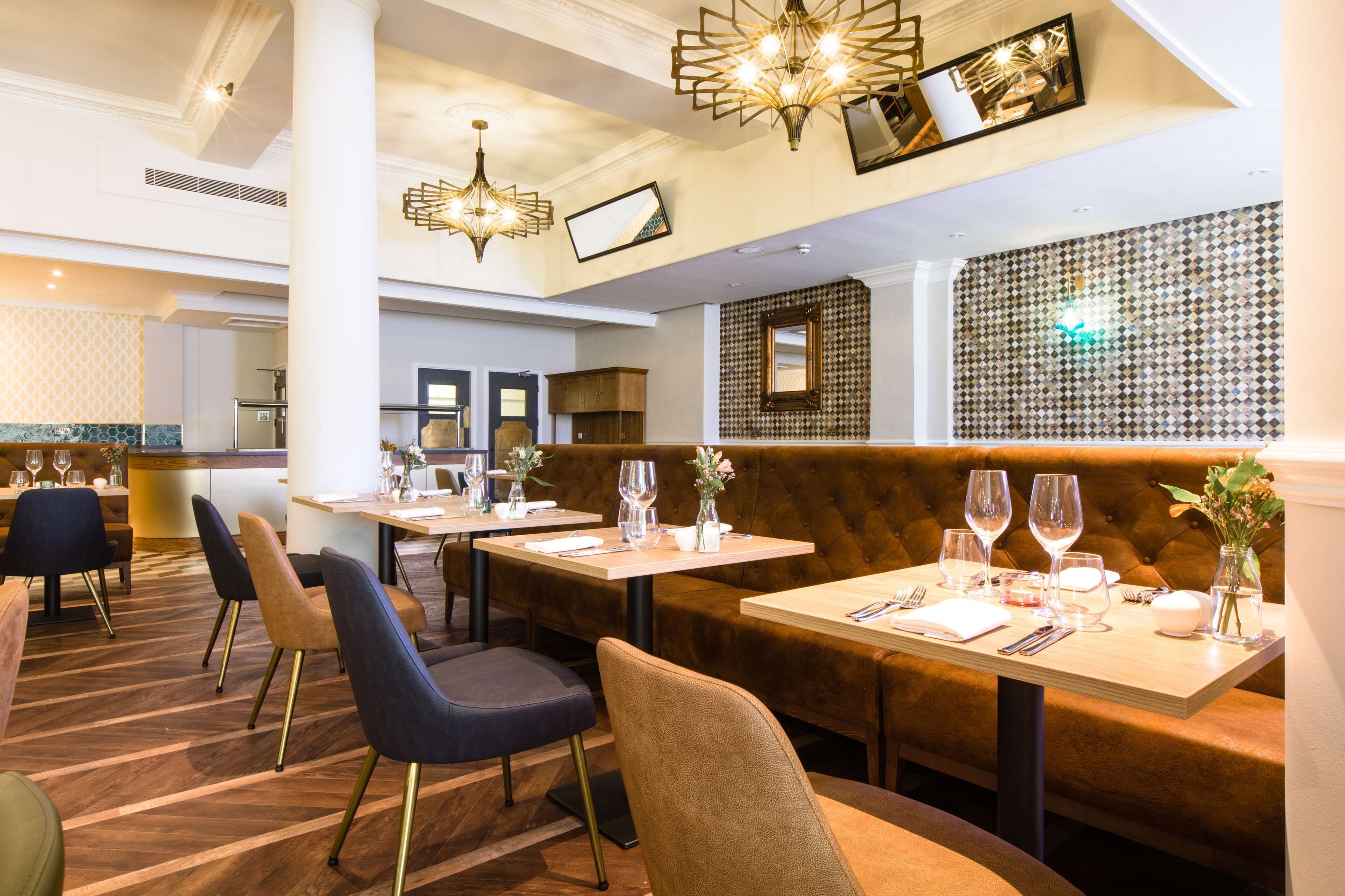 A restaurant with wooden tables and cushioned booths, featuring a patterned wall and pendant lighting.