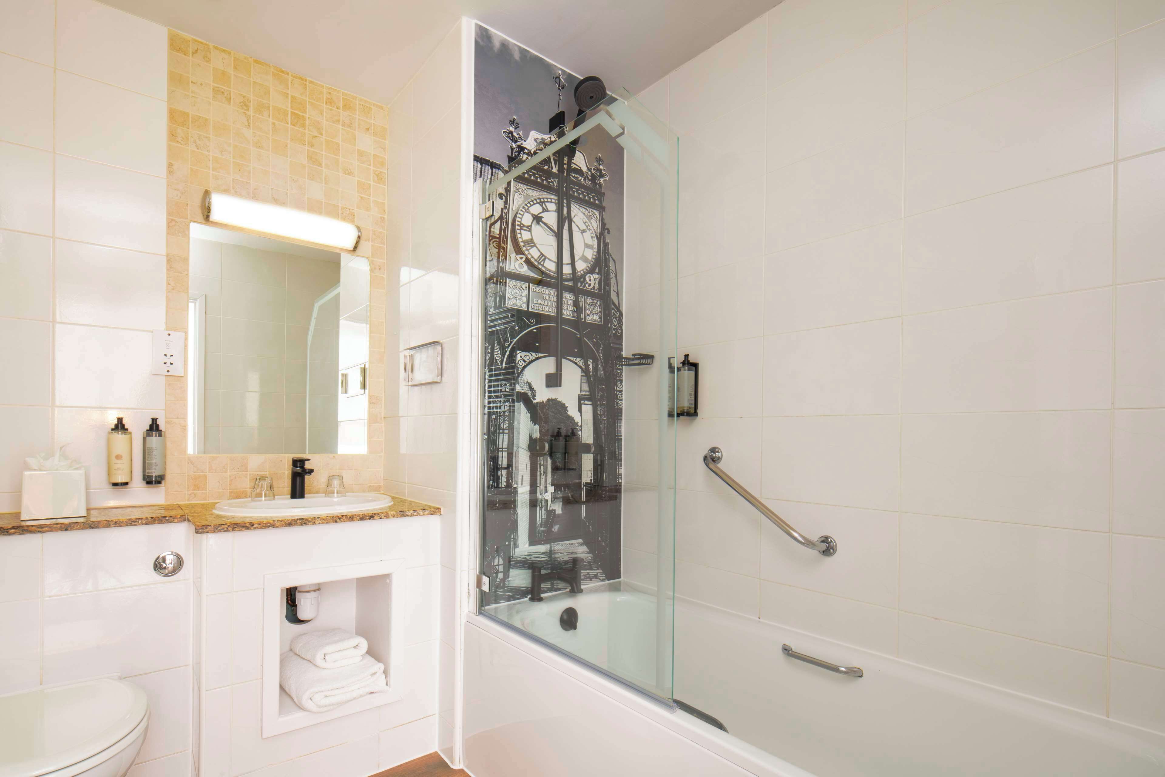 Un baño con ducha envuelta en vidrio, un lavabo blanco, un espejo y un perchero para toallas.