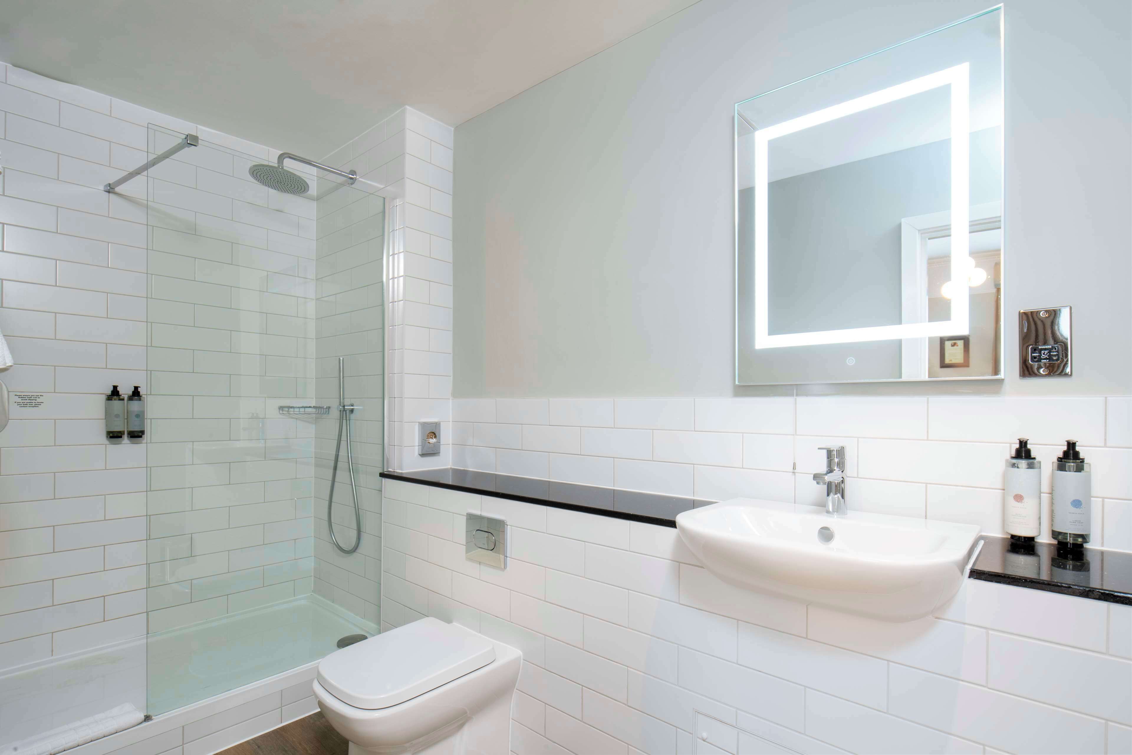 A modern bathroom with a glass-enclosed shower, a white toilet, and a sink with a mirror above it.
