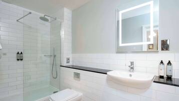 A modern bathroom with a glass-enclosed shower, a white toilet, and a sink with a mirror above it.