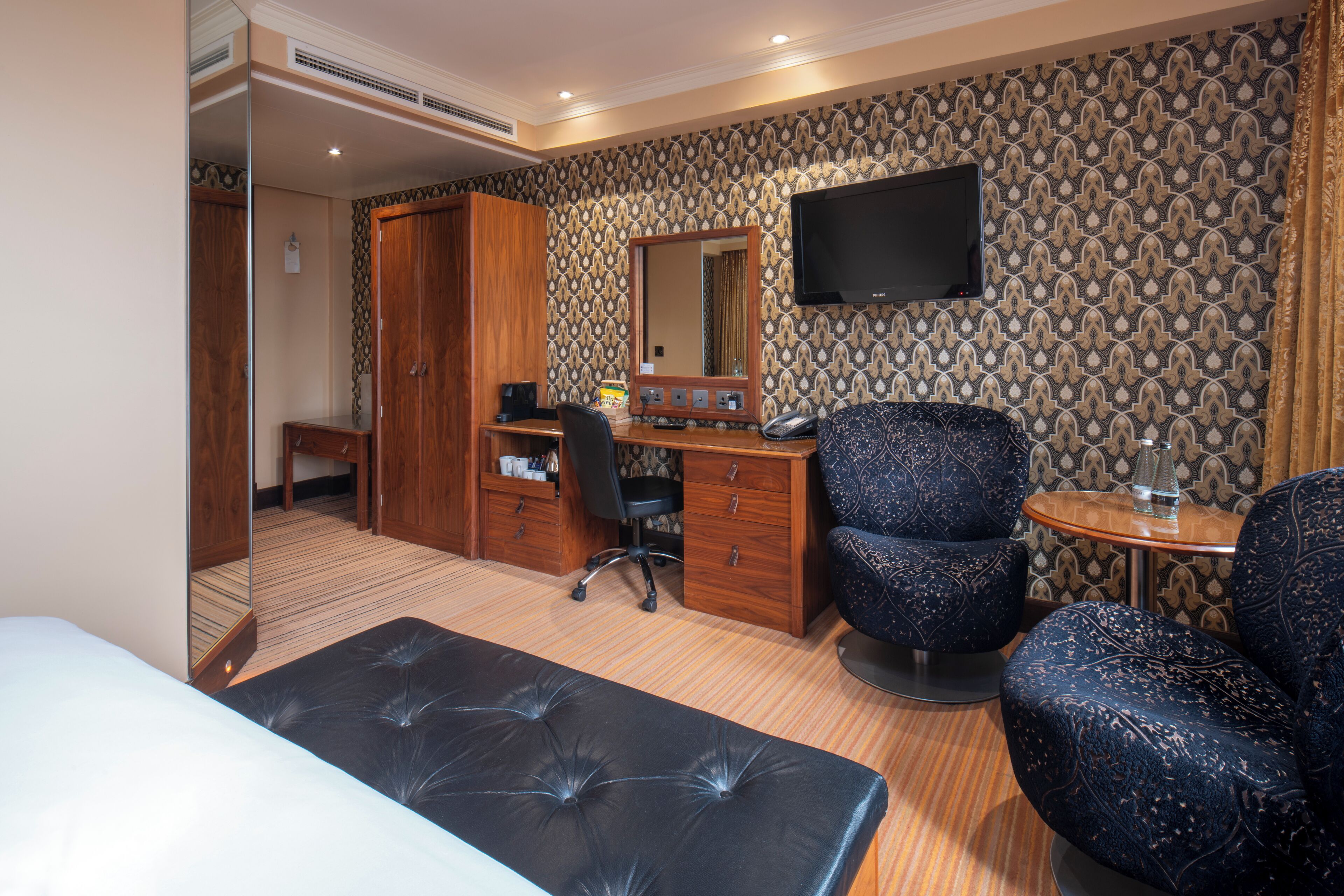 A hotel room with a bed, a desk, a chair, a TV, and a wardrobe.