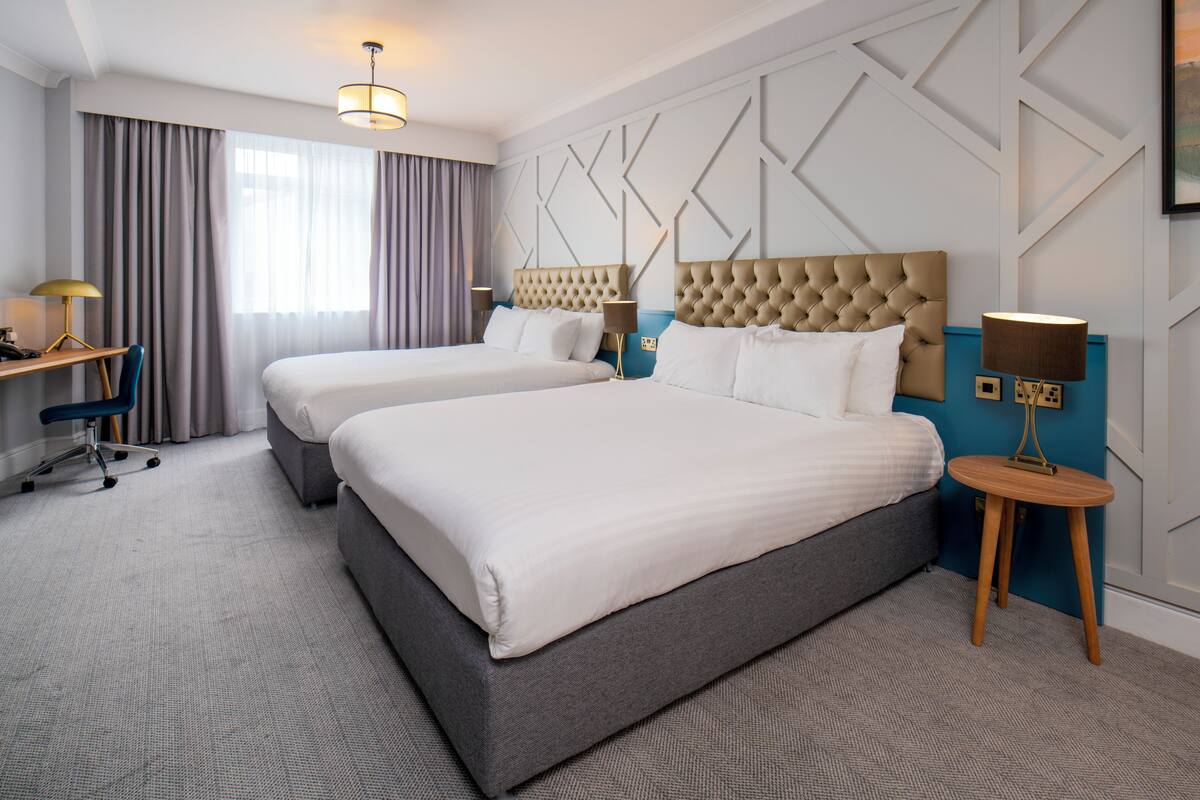A hotel room with two beds, a desk, and a chair.