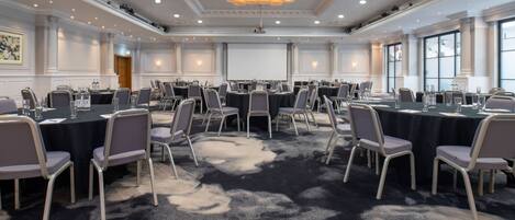 A conference room with round tables, chairs, a projector screen, and a carpeted floor.