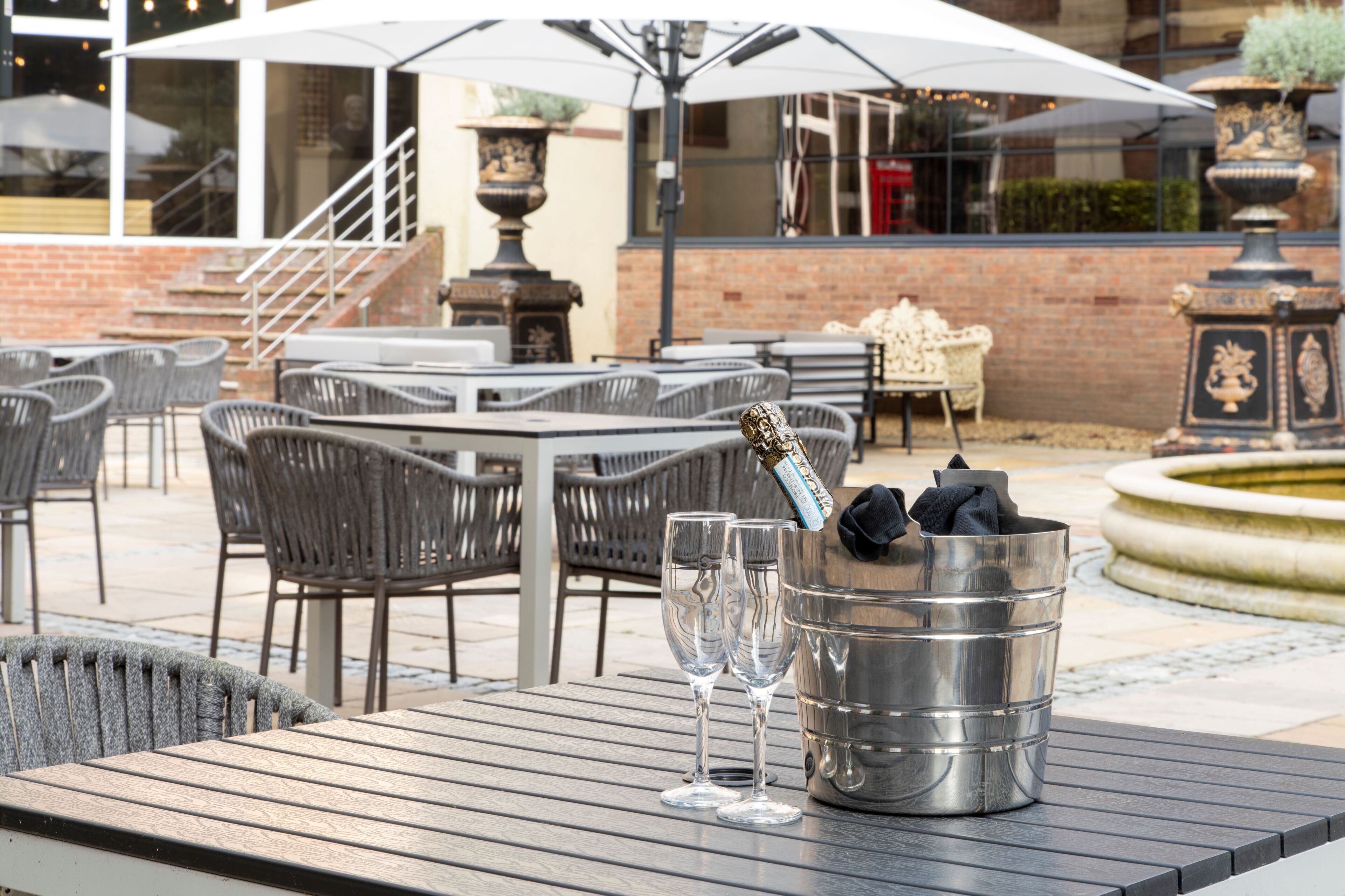 An outdoor patio with tables and chairs, a metal bucket with glasses, and a staircase leading to an upper level.