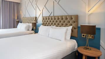 Una habitación de hotel con dos camas, un cabecero capitonado, una mesita de madera redonda y una lámpara de pared.