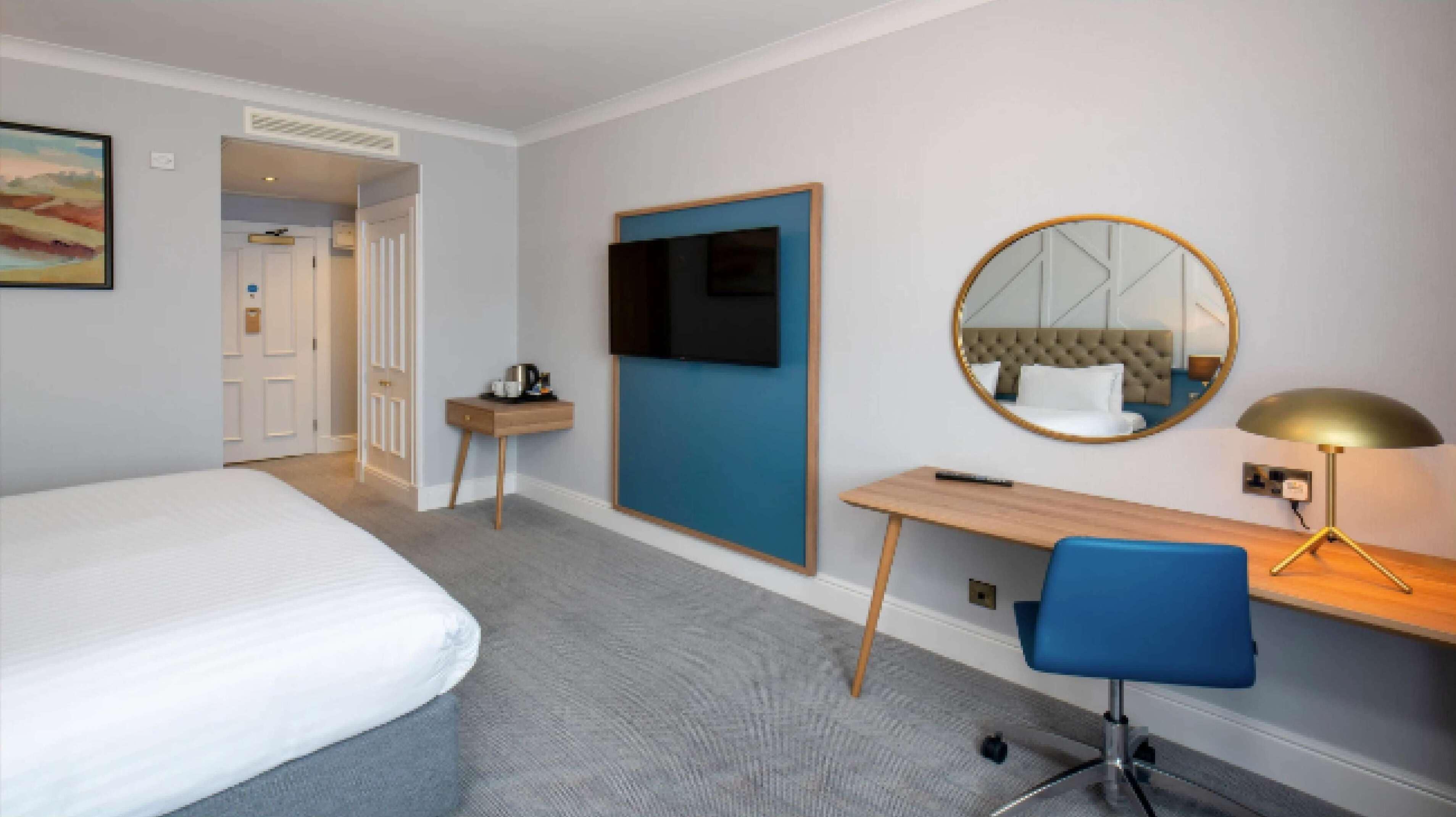 Une chambre d’hôtel équipée d’un lit, d’un bureau, d’une chaise, d’une télévision, d’un miroir et d’une lampe.