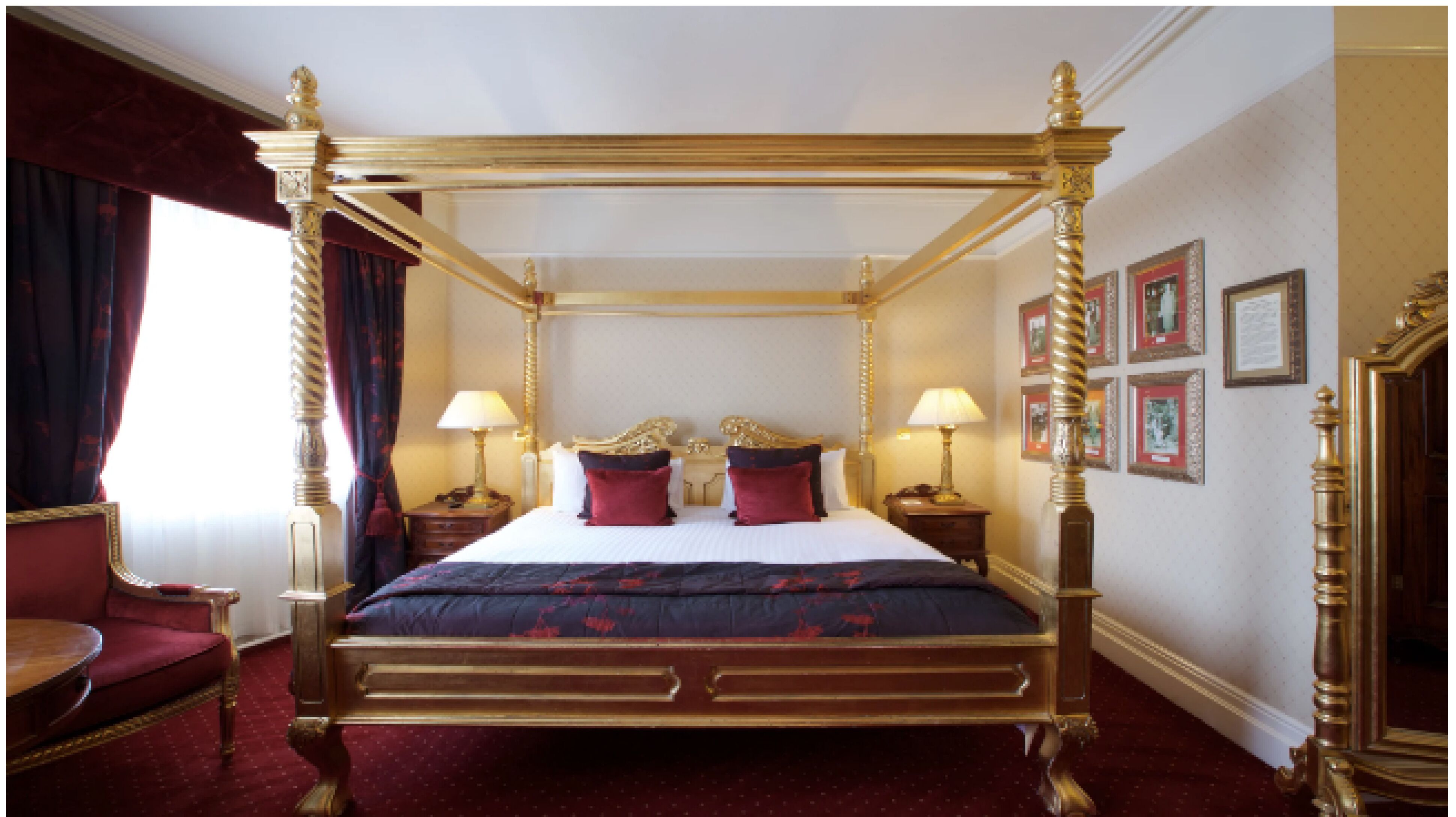 Una cama con dosel, dos mesitas de noche, un sillón tapizado en rojo y cuadros enmarcados en la pared.