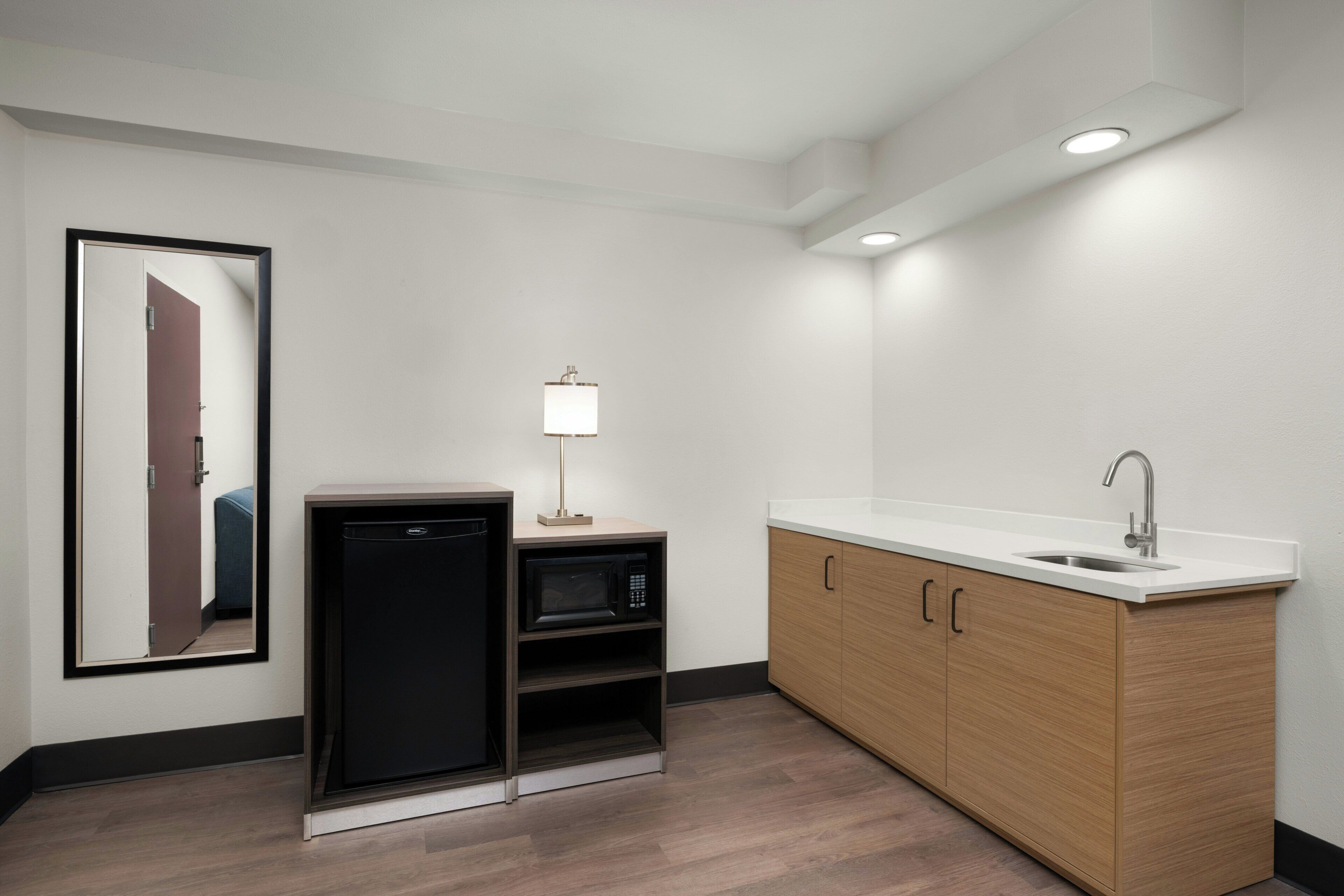 Una kitchenette compacta con microondas, un refrigerador pequeño, un lavamanos y un armario.