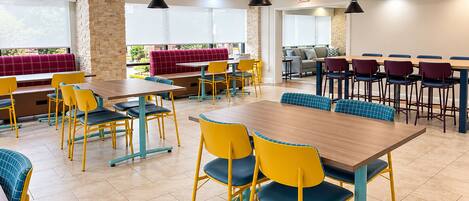 Un espace de restauration moderne, doté de plusieurs tables et chaises, d’un pilier en pierre et offrant une vue sur l’extérieur grâce à de grandes fenêtres.