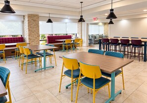 A modern dining area with multiple tables and chairs, a stone pillar, and a view through large windows. - Garner Hotel August West by IHG (Augusta)