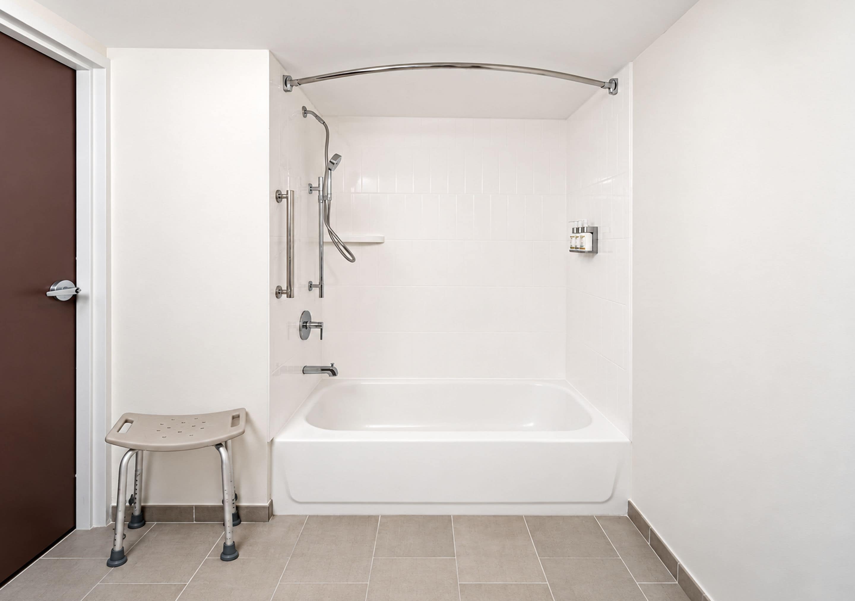 A bathroom with a white bathtub, a shower with a curved glass door, and a small step stool.