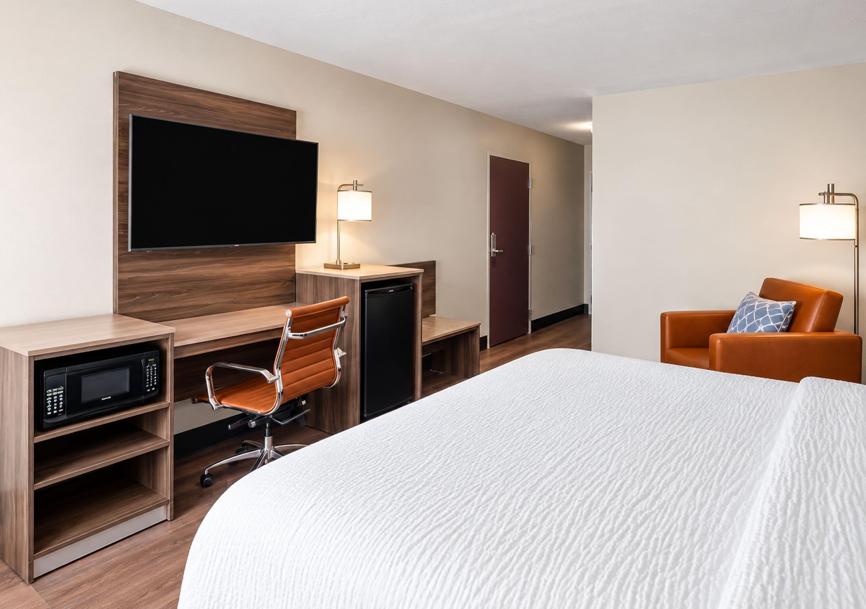 Une chambre d’hôtel avec un lit, un bureau équipé d’un ordinateur et d’un four à micro-ondes, une chaise, un téléviseur et une porte.