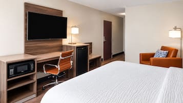 Ein Hotelzimmer mit einem Bett, einem Schreibtisch mit Computer und Mikrowelle, einem Sessel, einem Fernseher und einer Tür.
