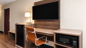 A hotel room with a desk, a chair, a television, a lamp, a microwave, and a mini-fridge.
