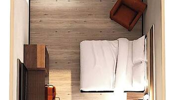 A compact hotel room with a bed, bedside table, lamp, and a small seating area.