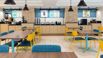 A cafeteria with tables and chairs, a coffee machine, and a menu board.