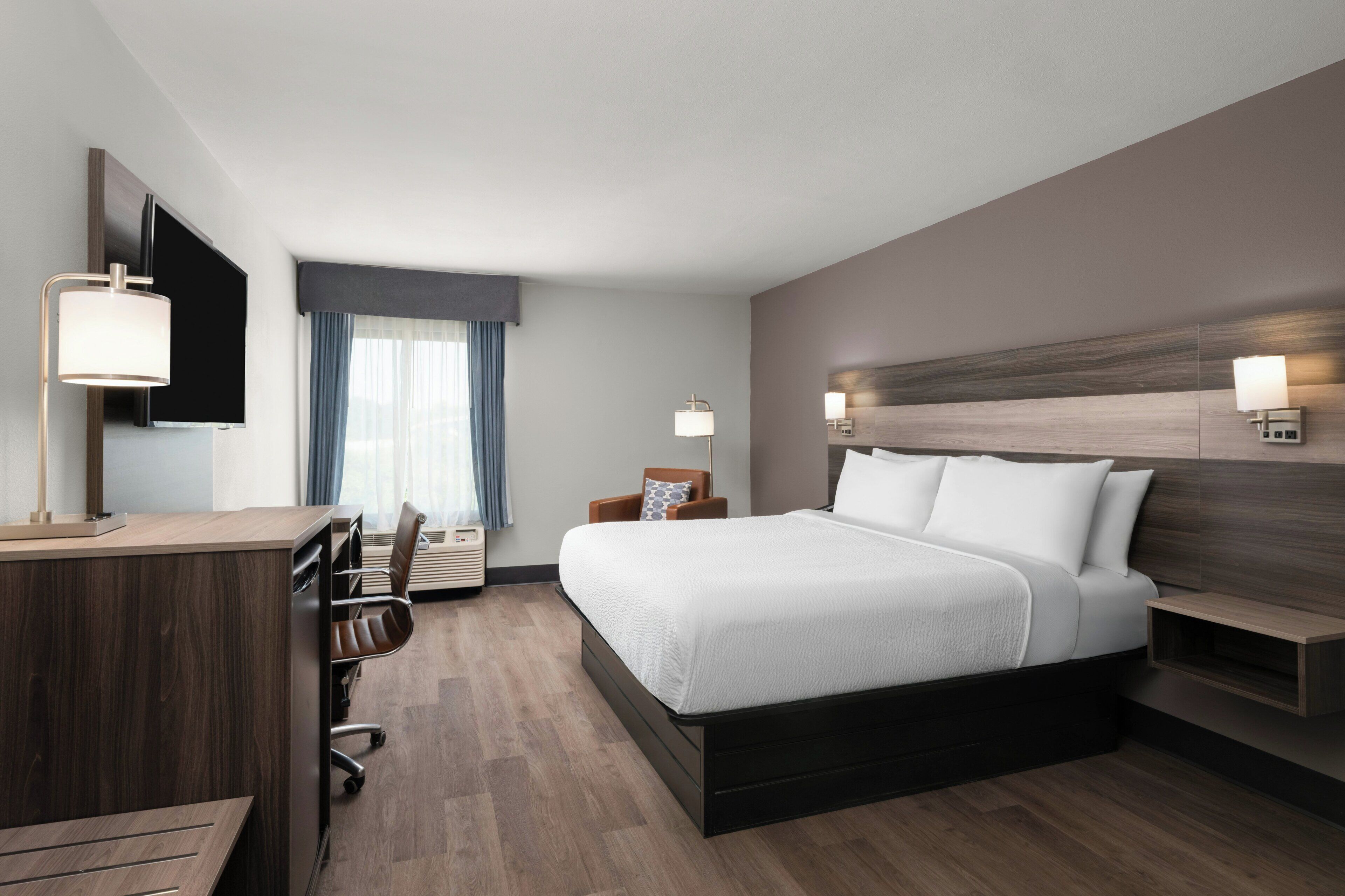 A hotel room with a bed, desk, chair, and a television.