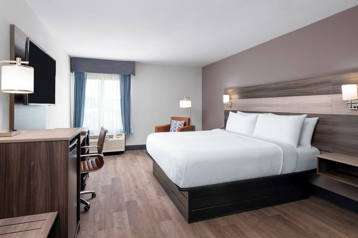 Habitación de hotel con una cama grande, un escritorio con silla, un televisor y una ventana con cortinas.