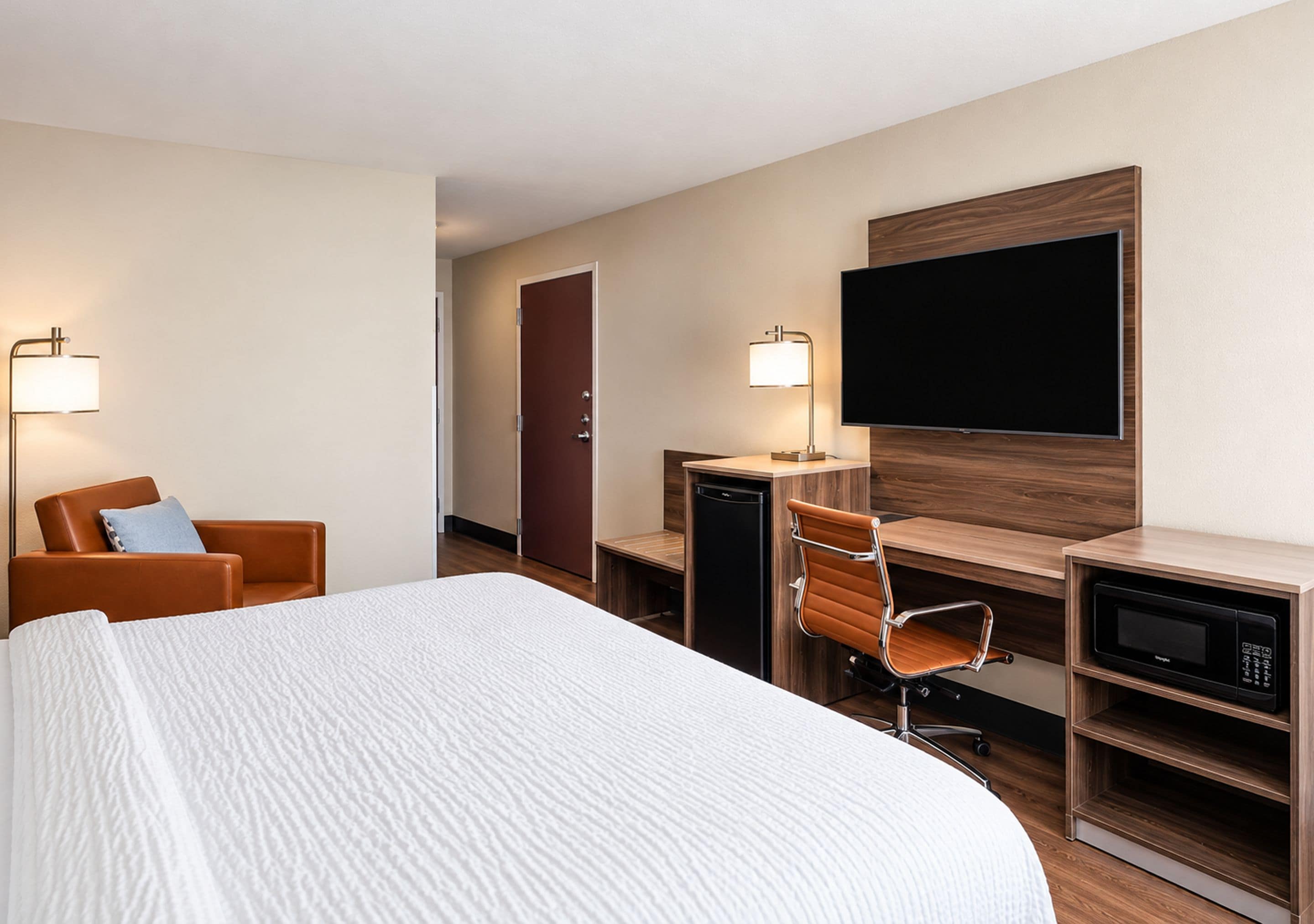 Een hotelkamer met een bed, een bureau, een stoel, een televisie en een magnetron.