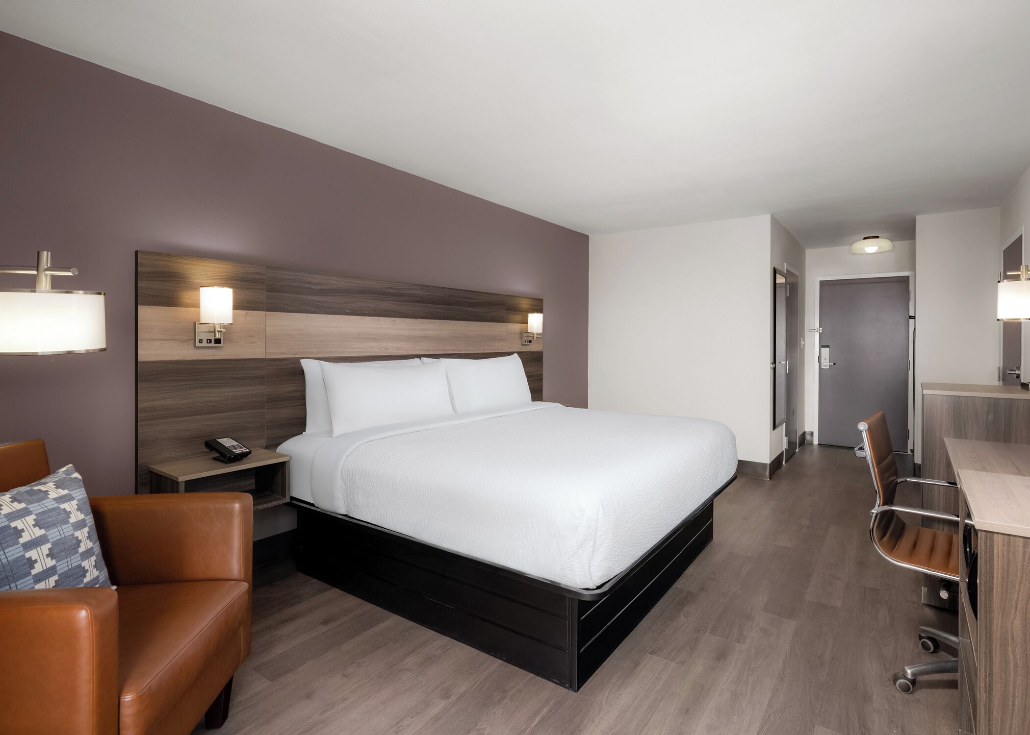 A modern hotel room with a large bed, a desk, a chair, and a nightstand with a phone.