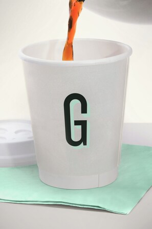 Una taza blanca con un logo 'G' negro sobre una superficie verde.