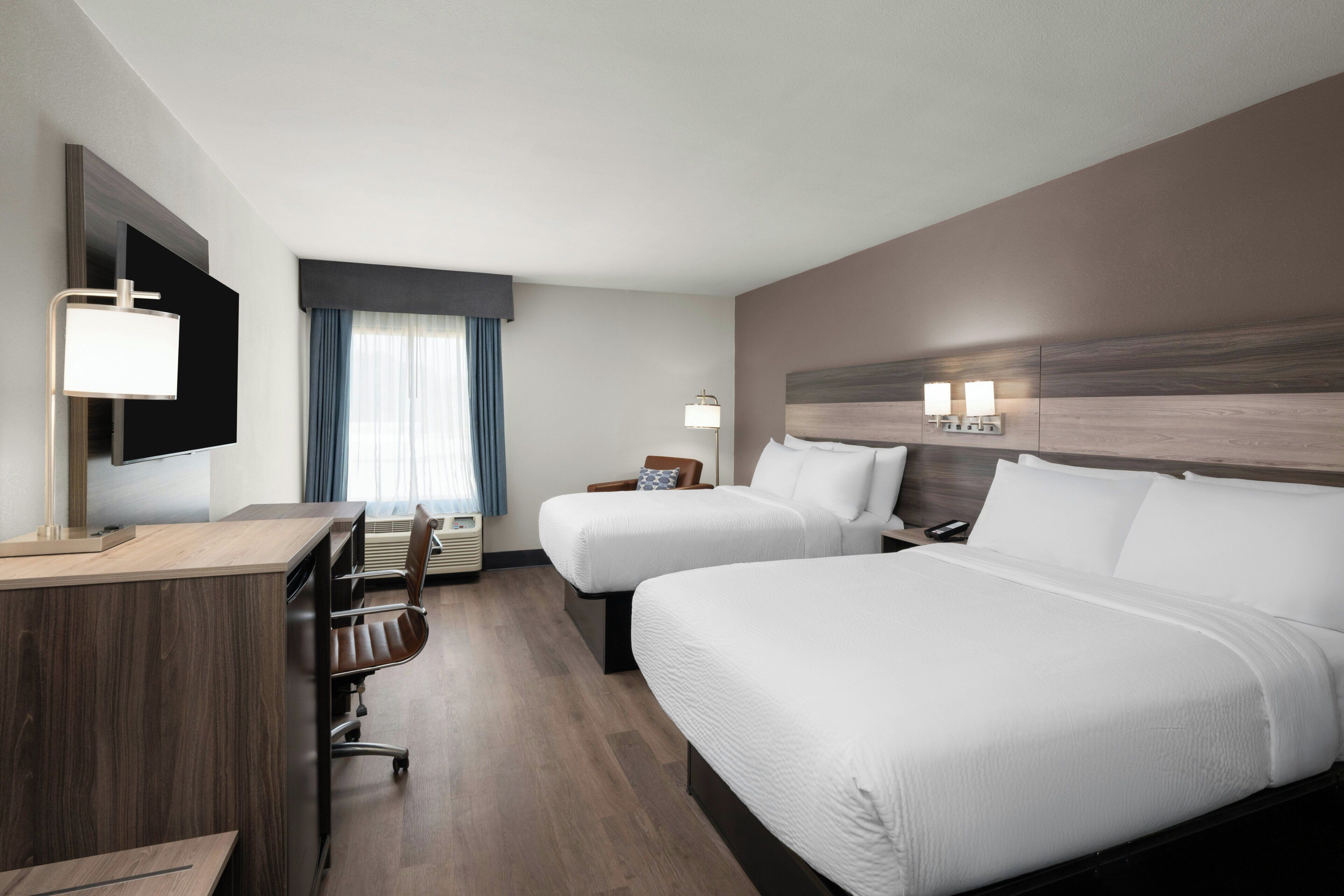 A hotel room with two beds, a desk, a chair, a TV, and a window with curtains.