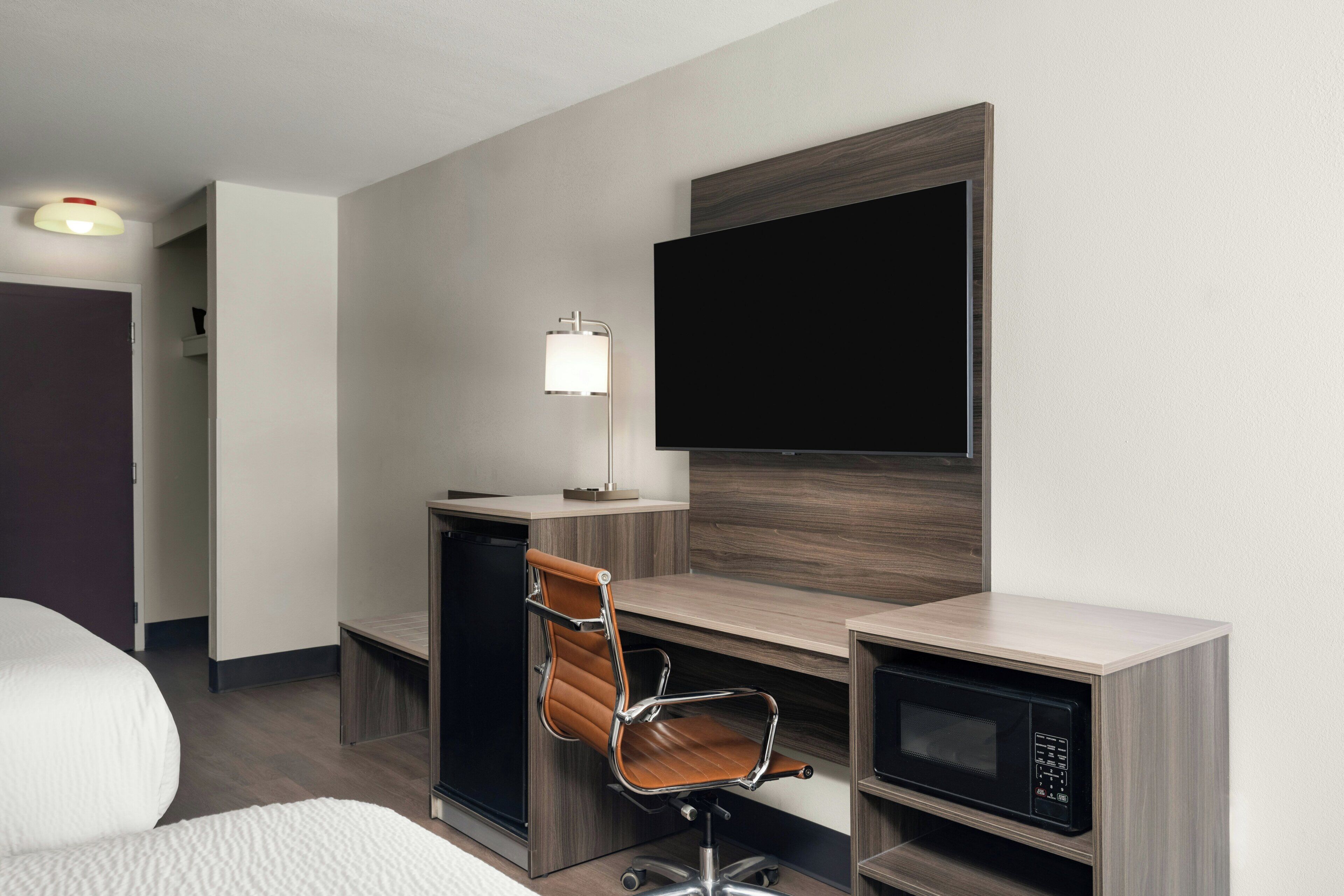 A hotel room with a desk, chair, television, and microwave.