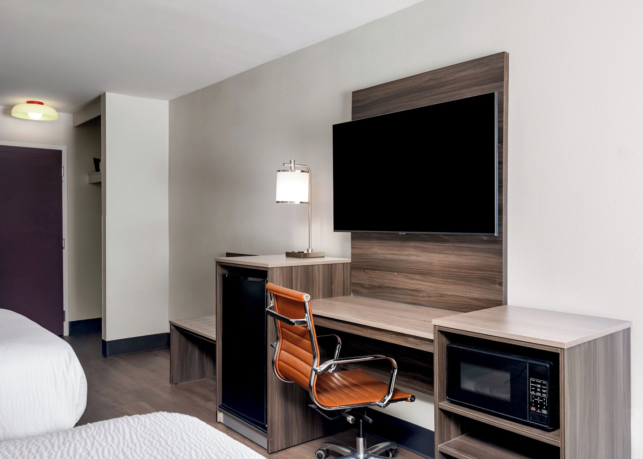Habitación de hotel con escritorio, silla, televisión, lámpara y microondas.
