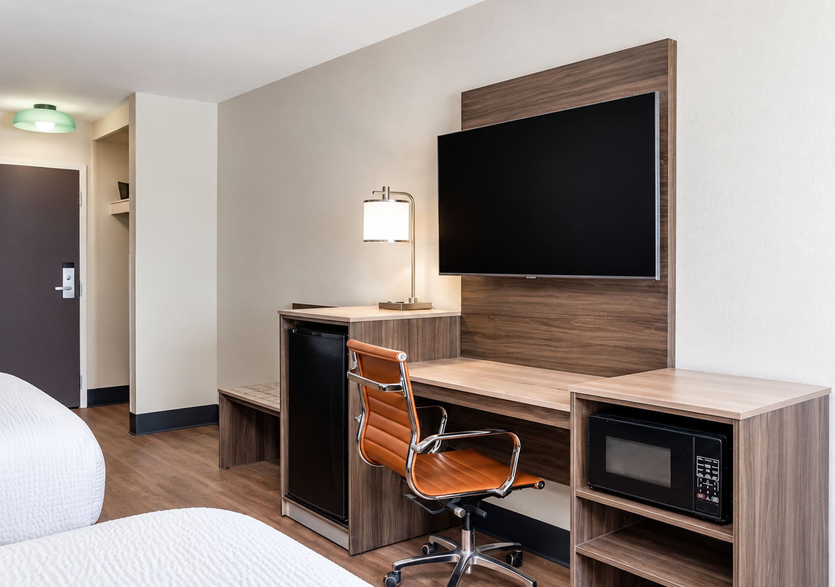 A hotel room with a desk, chair, television, and a microwave.