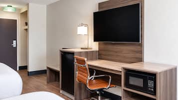 A hotel room with a desk, chair, television, and a microwave.